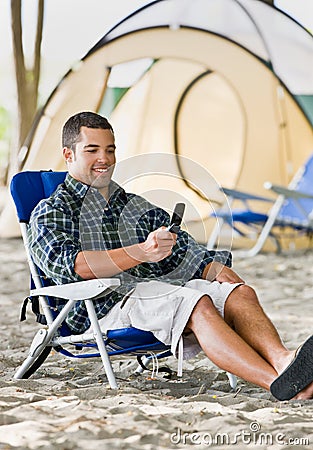 Man text messaging on cell phone at campsite Stock Photo