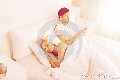 Man texting message while woman is sleeping in bed Stock Photo