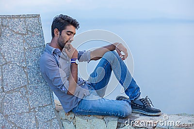 Man thinking sitting on a concrete bridge above the sea Stock Photo