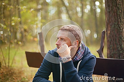 Man thinking moody portrait, sitting at autumn park Stock Photo