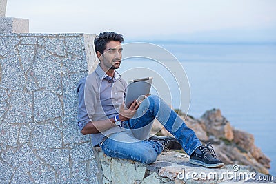 Man thinking using pad sitting on a concrete bridge above the sea Stock Photo