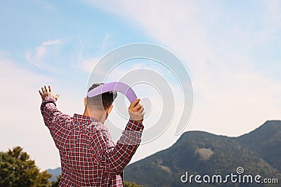 Man throwing boomerang in mountains on sunny day, back view. Space for text Stock Photo