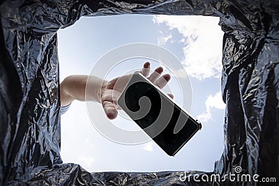 Man throws a non-working smartphone into a trash can. Bottom view from the trash can. The problem of recycling and pollution of Stock Photo