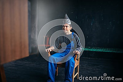 Man in tinfoil hat sits in chair, paranoia concept Stock Photo