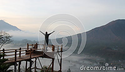 Man on top of mountain. Young man standing on the height of a wooden bridge, raised hands & open arms against mountain scenery. Editorial Stock Photo