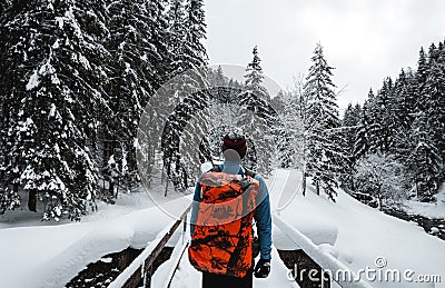 Man tourist and climber with orange backpack standing on the bridge with amazing view on snowy mountains in cold winter time. Editorial Stock Photo