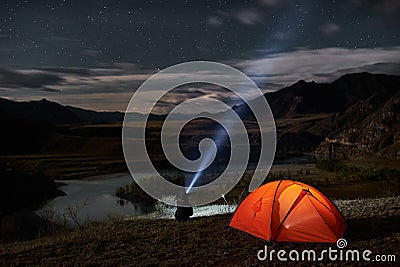 Man tourist with flashlight near his camp tent at night. Stock Photo