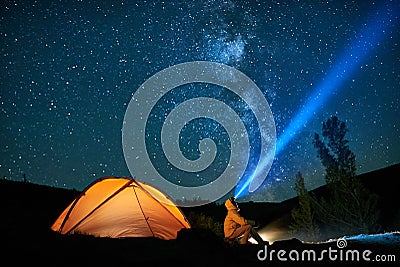 Man tourist with flashlight near his camp tent at night. Stock Photo