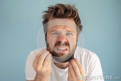 Man with a tousled hairstyle and an untidy beard, touches his stubble on his face, he is annoyed and dissatisfied with Stock Photo