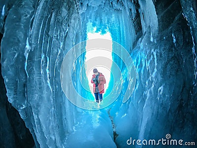 man traveler in orange jacket with camera in icicle frozen cave foreground Editorial Stock Photo