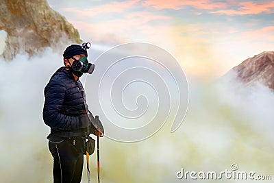 Man traveler in the crater of active volcano Ijen. Sulfur rocks, volcanic blue toxic lake and pink dawn. Gunung Ijen. Stock Photo