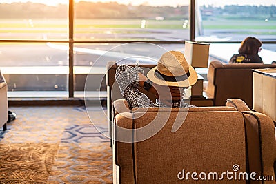 Man traveler with hat looking to airplane in the morning sunrise, Asian passenger sitting and relax in modern lounge at Stock Photo