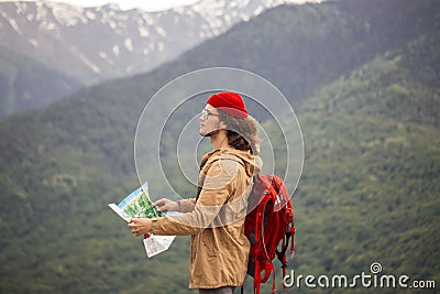 Man Traveler with map and red backpack searching location outdoor with rocky mountains on background Stock Photo