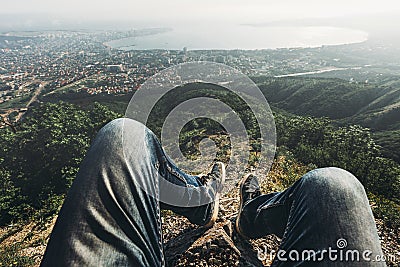 Man traveler sits on top and enjoys view of the picturesque landscape and the city. Point of view shot. Travel, adventure, tourism Stock Photo