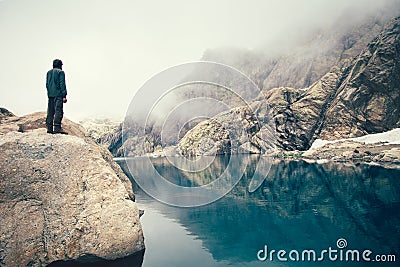 Man Traveler standing alone on stone cliff lake and misty mountains on background Stock Photo