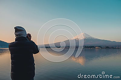 Man traveler standing and taking photo Beautiful Mount Fuji with snow capped in the morning sunrise at Lake kawaguchiko, Japan. Editorial Stock Photo