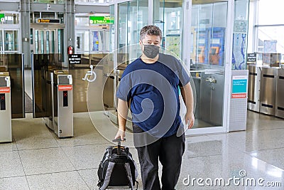 Man traveler with suitcase on wheels wears protective mask during pandemic outbreak afraids of dangerous influenza coronavirus Stock Photo