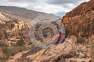 A man traveller sitting on rock and looking to landscape of Wadi Musa in Petra ruin and ancient city in Jordan Editorial Stock Photo