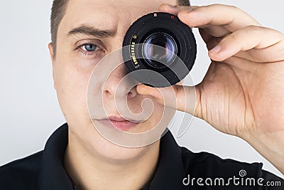 A man tries on a camera lens instead of an eye. The concept of the photographer`s work and the creative approach to photography Stock Photo