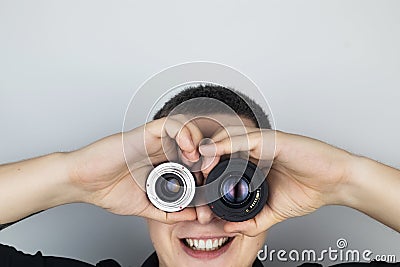 A man tries on two camera lenses instead of eyes. He plays around and fools around. The concept of the photographer`s work and th Stock Photo