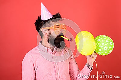 Man with trimmed beard wearing pink shirt and party cap on red background. Bearded man blowing party whistle Stock Photo