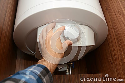 Man turn off electric hot water boiler as a concept of energy crisis. Electric boilers provide heating and hot water for a Stock Photo