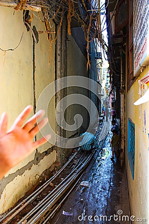 Delhi, India - August 18, 2009: man and two child in a very narrow alley of delhi full of rubbish, exposed pipes, electric cables Editorial Stock Photo