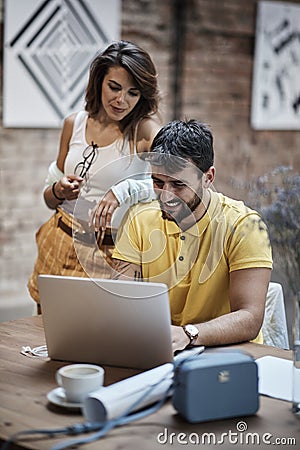 Man typing on laptop, smiling, with beautiful female leaned on his shoulder Stock Photo
