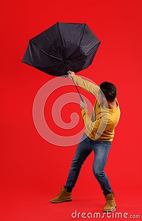 Man with umbrella caught in gust of wind on red background Stock Photo