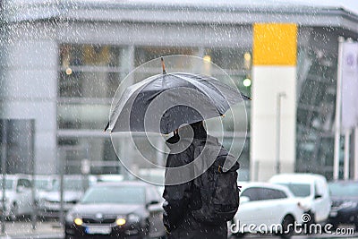 A man with an umbrella in the rain crossing the road. Stock Photo