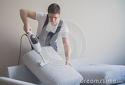 Man in uniform cleaning sofa. Stock Photo