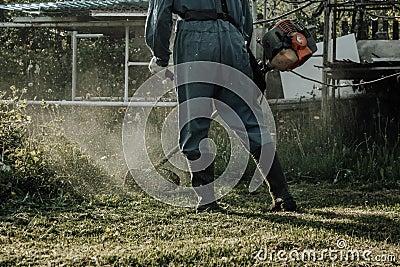 Man in uniform mowing grass with electric mower. The felling of the weed Stock Photo