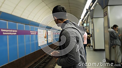 Man uses tablet in subway. Media. Young man uses tablet while waiting for train in metro. Young man is waiting for metro Stock Photo