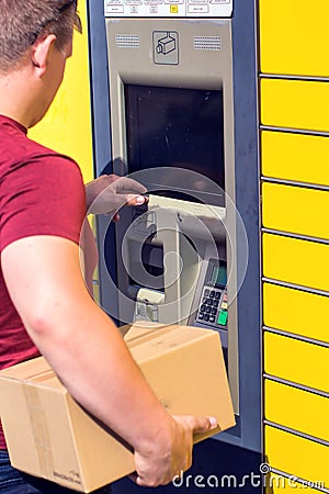 Man client using automated self-service post terminal machine or locker to depisit a parcel for storage Editorial Stock Photo