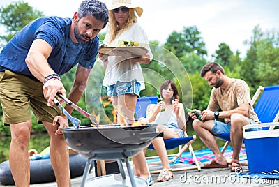 Man using bellows for preparing food in barbecue grill with friends on pier Stock Photo