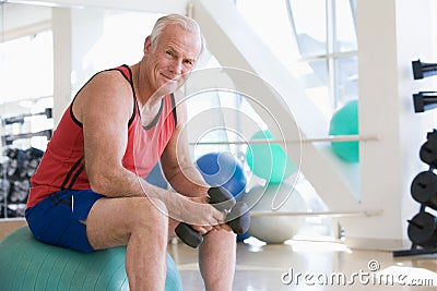 Man Using Hand Weights On Swiss Ball At Gym Stock Photo