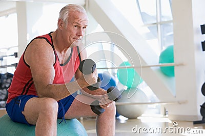 Man Using Hand Weights On Swiss Ball At Gym Stock Photo