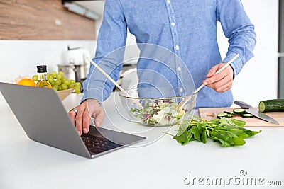 Man using laptop and making salad in glass bowl Stock Photo