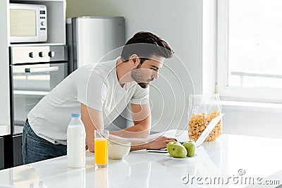 Man using laptop near cereals, milk and orange juice Stock Photo