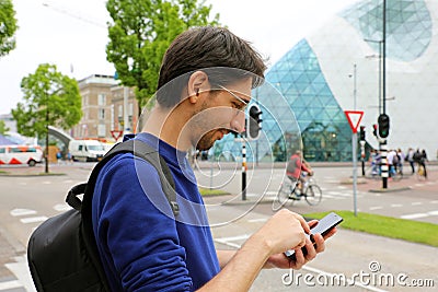 Man using mobile phone app in modern urban city street. Young caucasian man holding smartphone for business work. Stock Photo