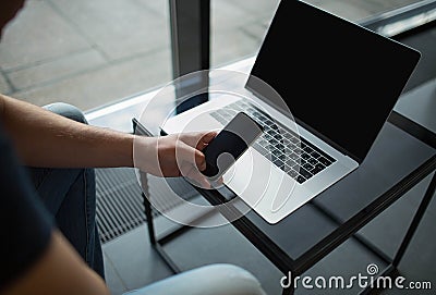 Man using modern mobile phone after work on laptop computer, sitting in office interior. Stock Photo