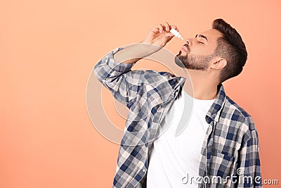 Man using nasal spray on peach background, space for text Stock Photo