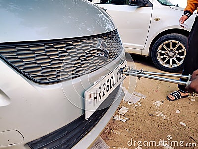 Man using a riveting locking tool to affix a tamper proof HSRP high security registeration plate to a maruti swift car Editorial Stock Photo