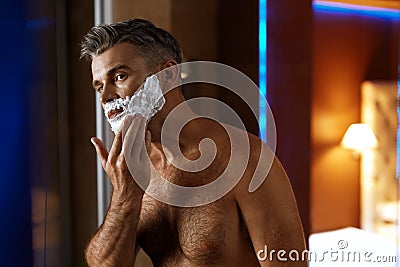 Man Using Shaving Cream On Face In Bathroom. Men Skin Care Stock Photo