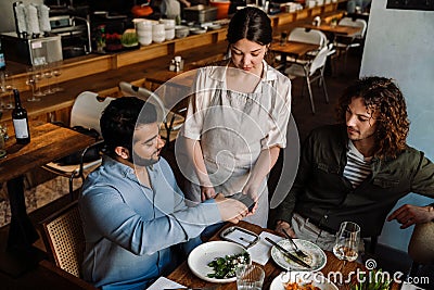 Man using smartphone while paying restaurant bill with contactless payment during dinner with friends Stock Photo