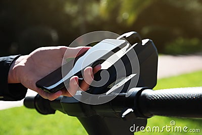 Man using smartphone to pay and unblock rental electric scooter outdoors, closeup Stock Photo