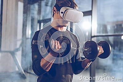 Man in virtual reality headset exercising with dumbbells in gym Stock Photo