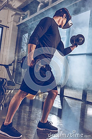 Man in virtual reality headset exercising with dumbbells in gym Stock Photo