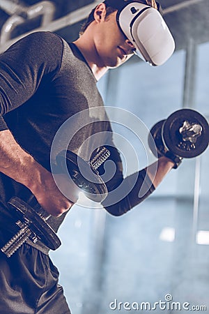 Man in virtual reality headset exercising with dumbbells in gym Stock Photo