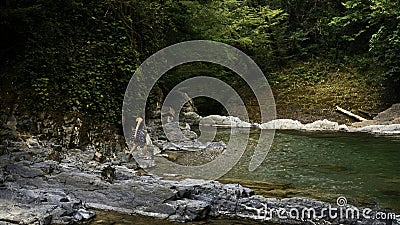 Man walking on the rocky river in paradise place. Creative. Woman cooling her feet in cld mountain stream. Stock Photo